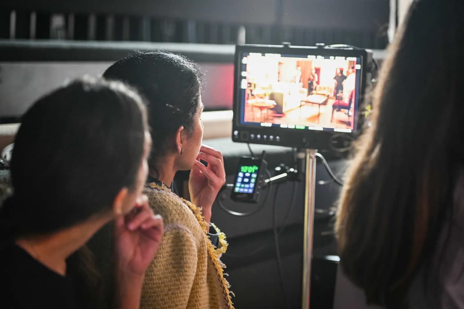 Two people, seen from behind, are looking at a monitor displaying a brightly lit interior scene, possibly from a film or television set.